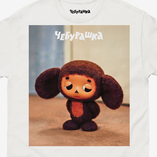 White unisex T-shirt with large print of original Sad Cheburashka from Soviet cartoon. With logo Чебурашка. Closeup photo.