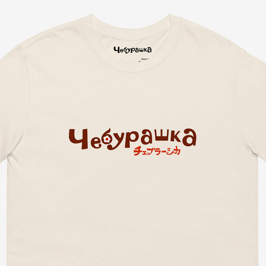 A beige short-sleeve unisex Cheburashka, original Soviet cartoon Tee with a brown 'Чебурашка' logo in russian and smaller underneath logo in japanese チェブラーシカ. Closeup print details.
