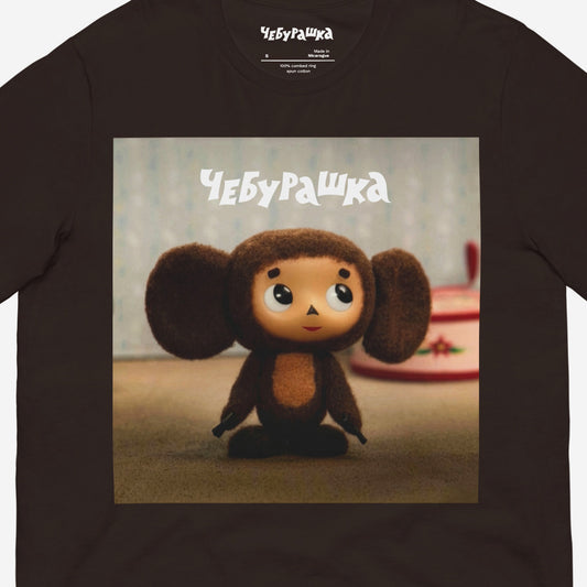 Brown unisex T-shirt with large print of original Soviet cartoon character Cheburashka standing cute and curious. Featuring Чебурашка logo at the of the print. Front closeup.