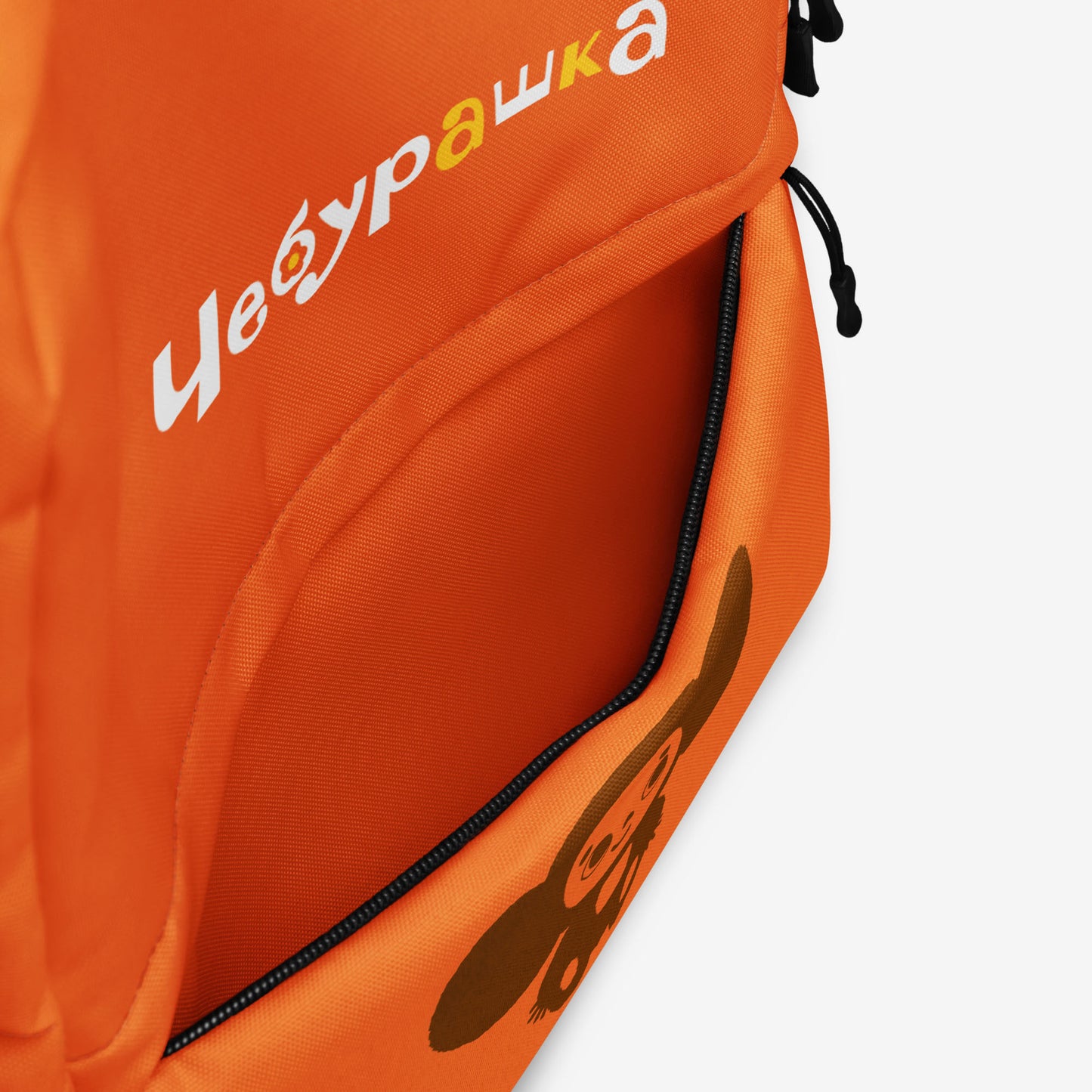 An orange backpack with a front pocket, featuring the Soviet cartoon character Cheburashka and logo 'Чебурашка' in white and yellow with flowers. Front pocket details.
