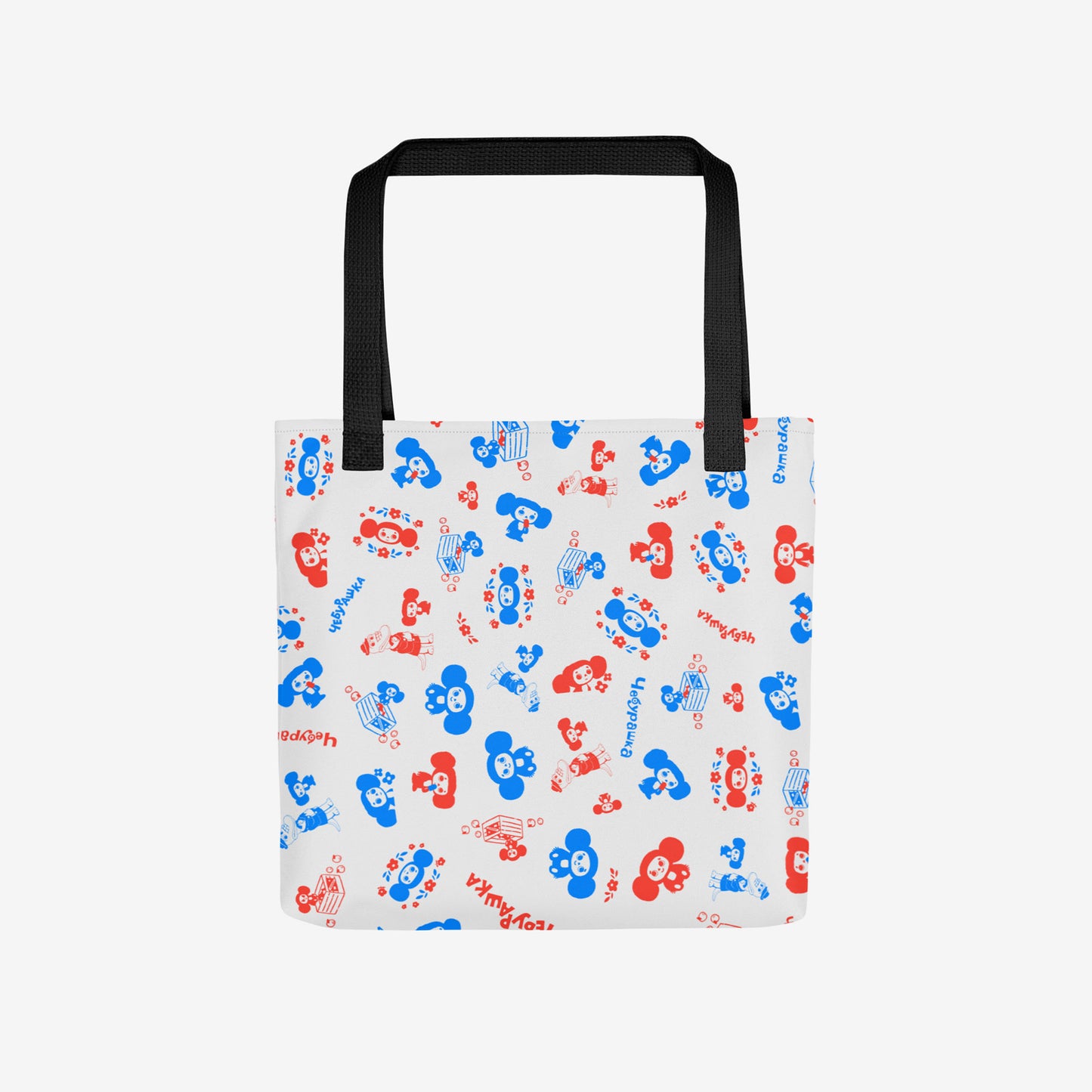 A white tote bag with a black shoulder strap, featuring an all-over pattern of red and blue original Soviet cartoon characters Cheburashka. Front photo.