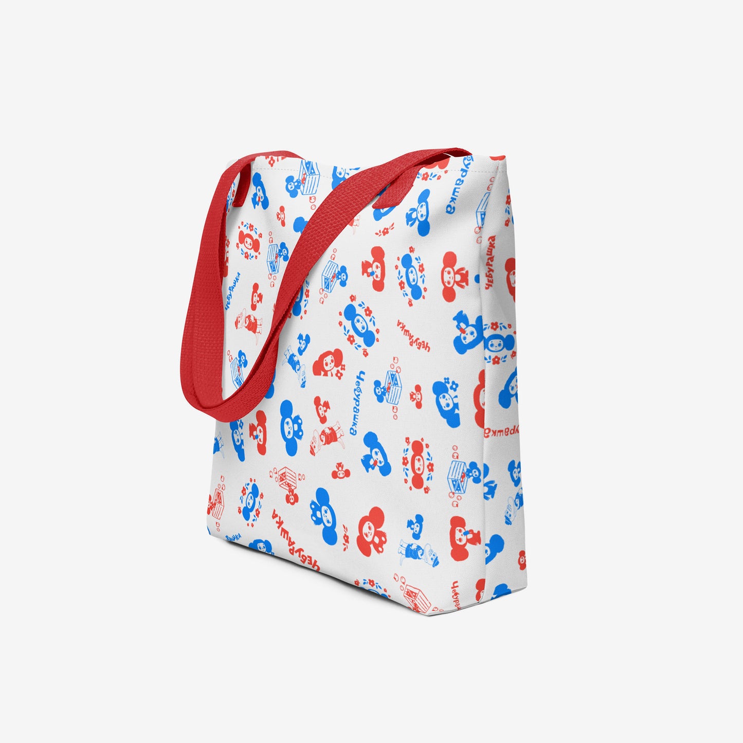 A white tote bag with a red shoulder strap, featuring an all-over pattern of red and blue original Soviet cartoon characters Cheburashka. Side photo.