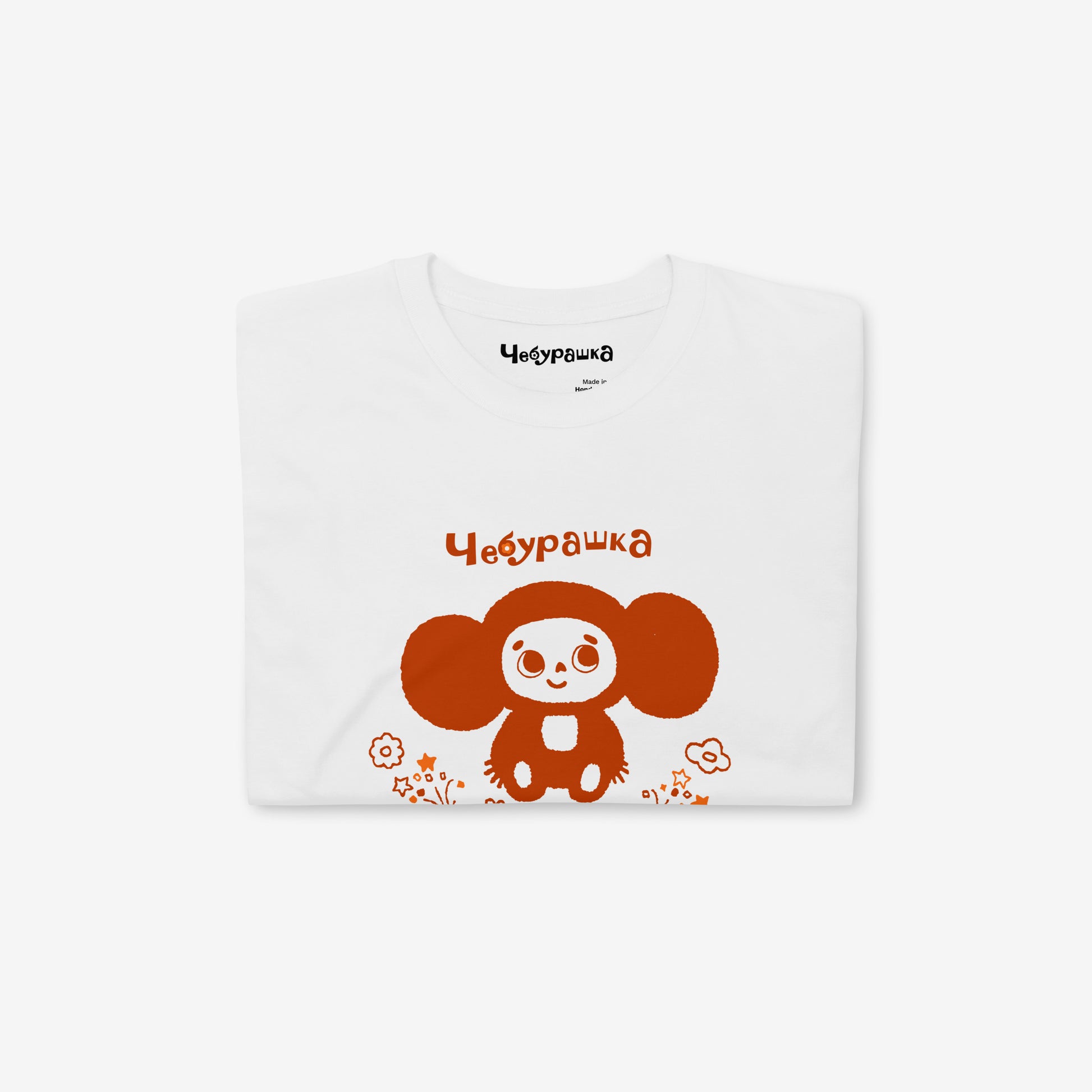 White unisex tee featuring minimalist brown Cheburashka with a birthday cake.  Folded. www.cheburashkashop.com