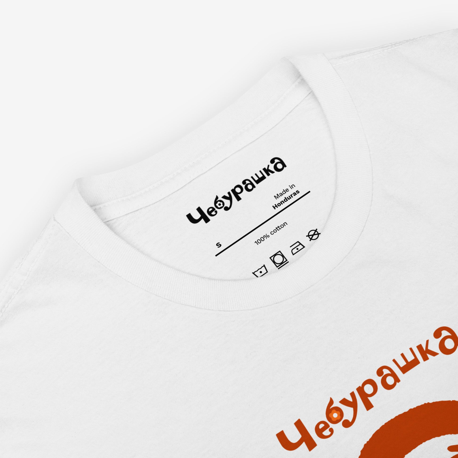 White unisex tee featuring minimalist brown Cheburashka with a birthday cake.  Closeup photo with Чебурашка logo on necktag. www.cheburashkashop.com