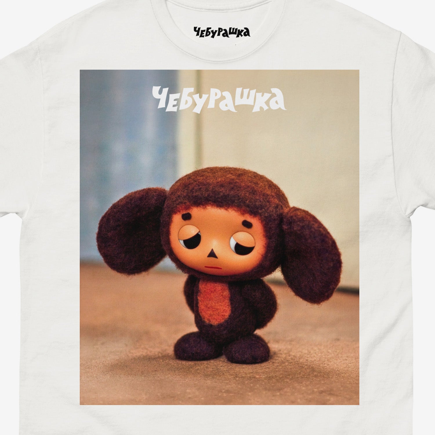 White unisex T-shirt with large print of original Sad Cheburashka from Soviet cartoon. With logo Чебурашка. Closeup photo.