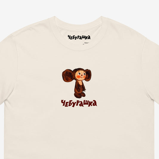Unisex natural-white Tee featuring original Soviet cartoon character clumsy painted Cheburashka and Чебурашка logo in brown. High-quality 100% cotton. Closeup.