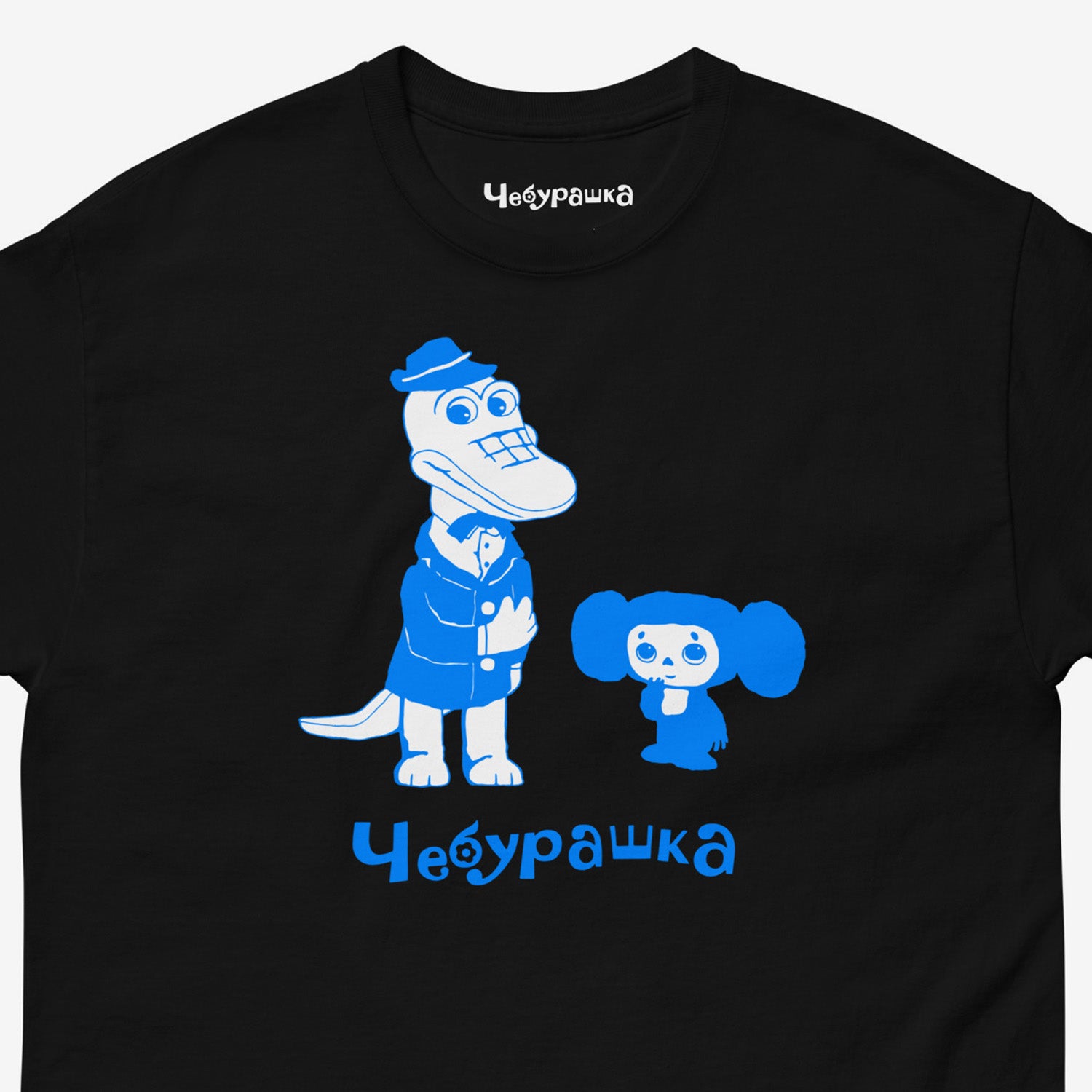 Black unisex adult tee featuring minimalist graphic of Cheburashka with his friend Gena the crocodile and text Чебурашка. Cute light-blue print color. With branded necktag logo Чебурашка. Closeup photo. www.cheburashkashop.com