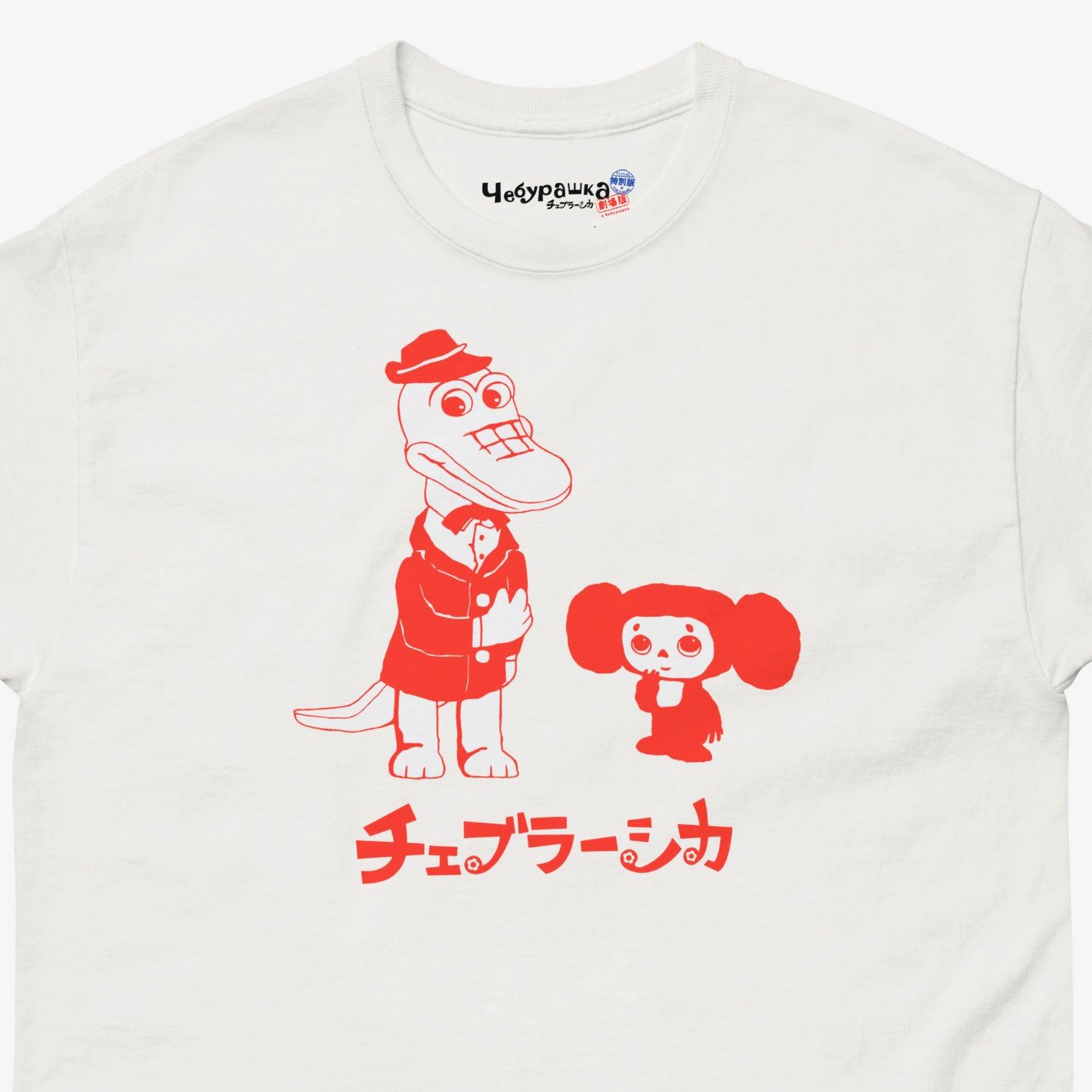 White unisex adult tee featuring minimalist red graphic of Cheburashka with his friend Gena the crocodile. Japanese edition with text チェブラーシカ. Cute red-pinkish print color. Branded necktag logo Чебурашка. Closeup photo. www.cheburashkashop.com