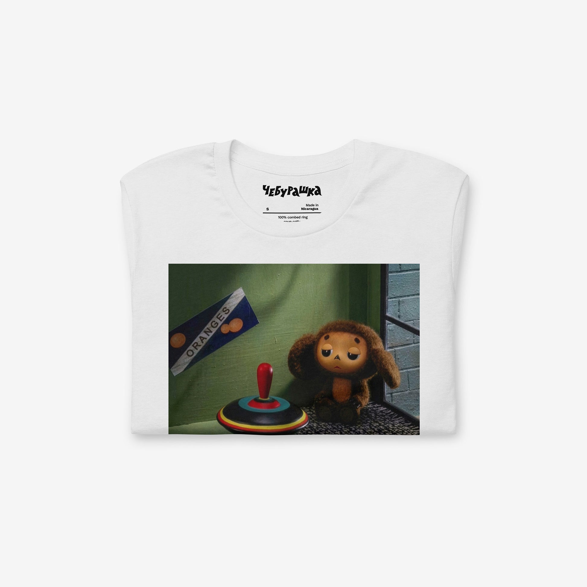 Unisex T-shirt with large print of original Soviet cartoon character Cheburashka sitting sad in phone booth and logo Чебурашка. 2013 edition. Folded.