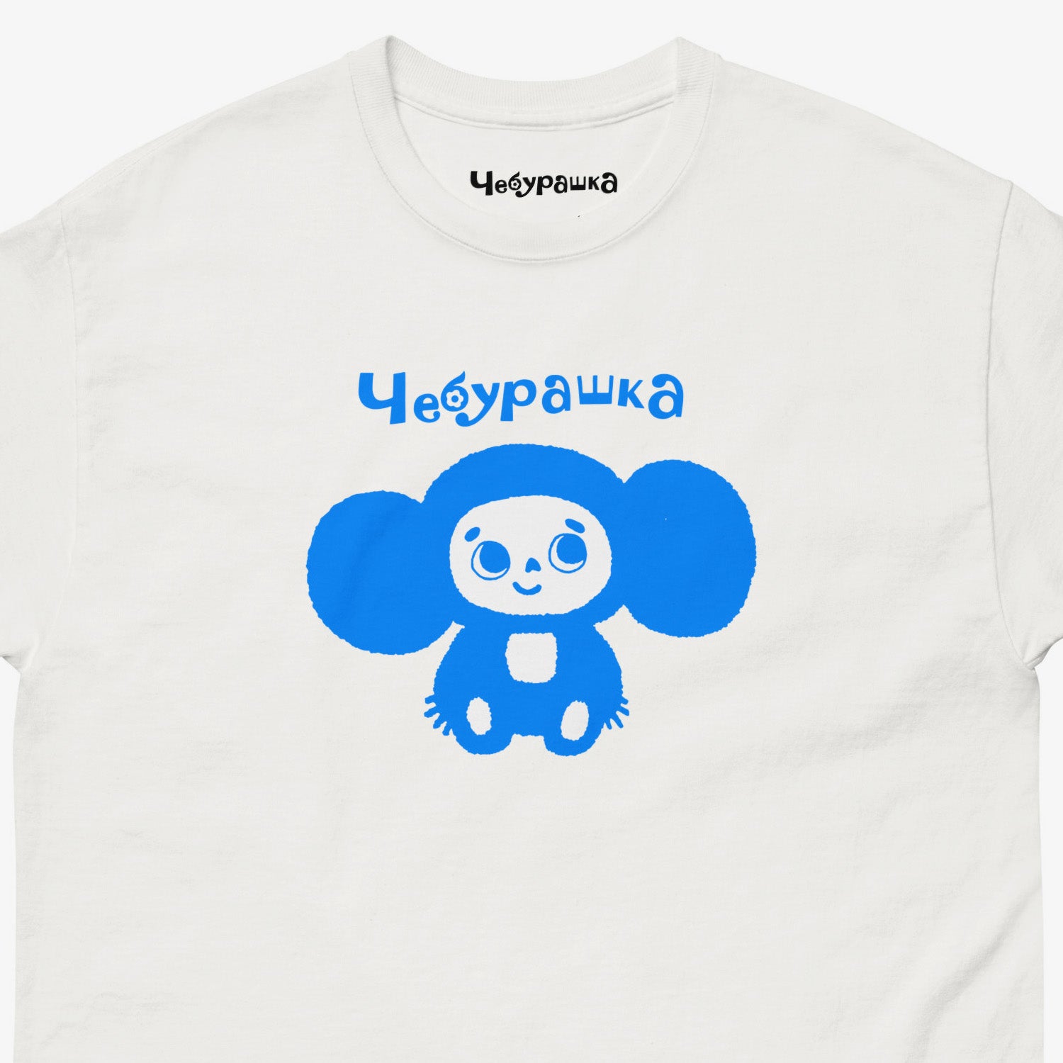 White unisex tee with original Soviet cartoon character Cheburashka. Lonely and smiley, in blue. Closeup.