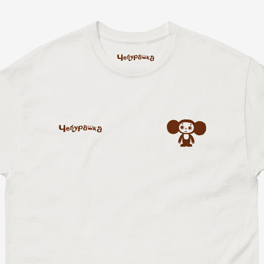 White unisex T-shirt featuring Soviet cartoon Cheburashka, standing and smiling. Discreet design with small cheburashka on the right and Чебурашка logo on the left. Closeup.