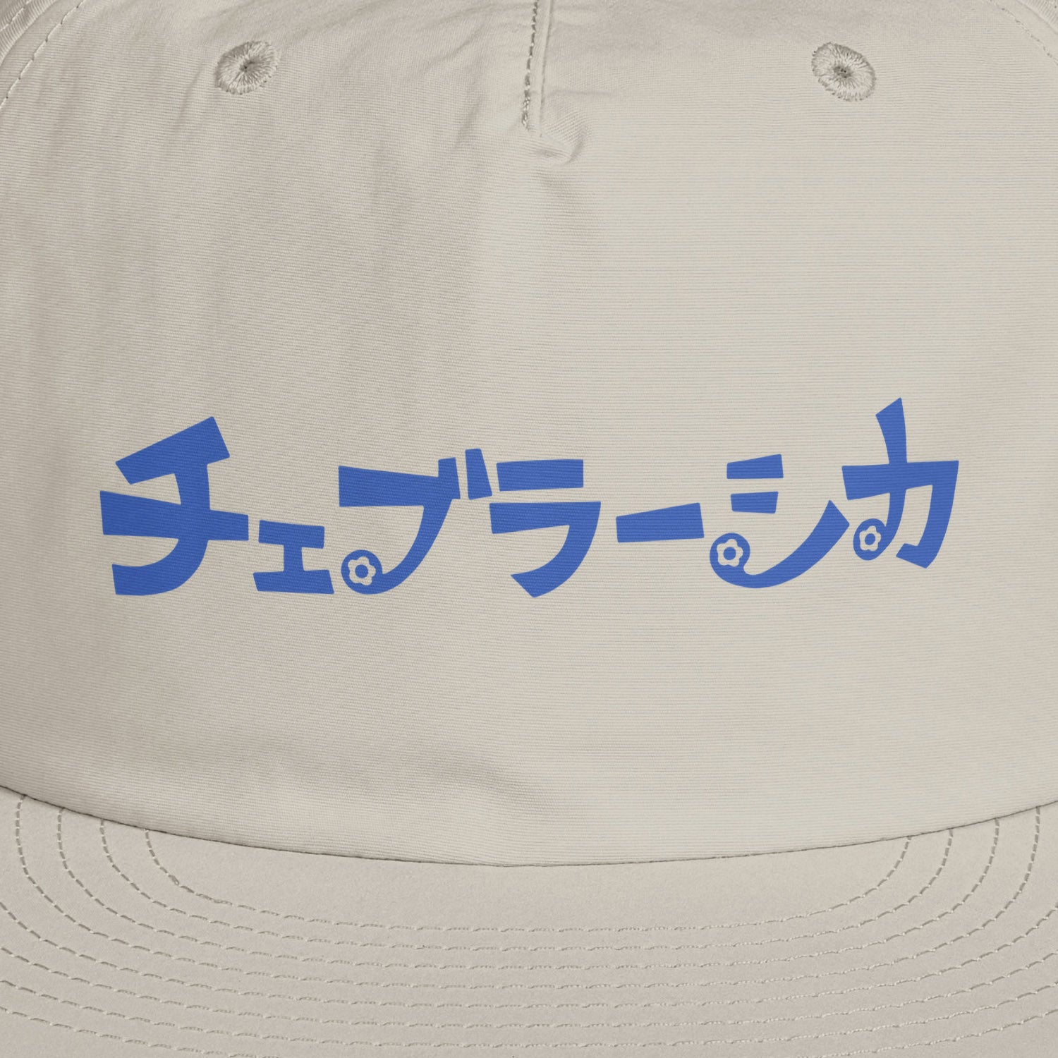 A light beige surf cap with a flat brim, featuring Cheburashka Soviet cartoon logo in japanese チェブラーシカ on the front. Front closeup.