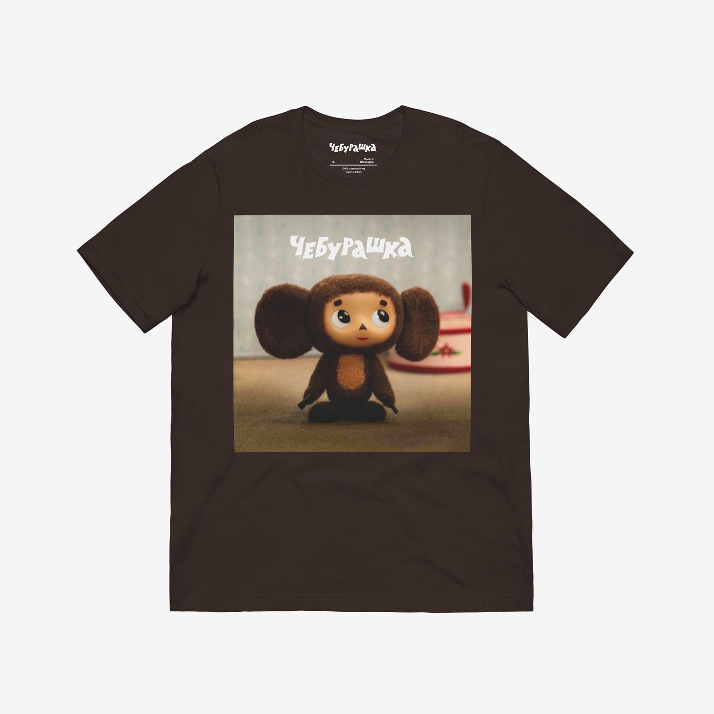 Brown unisex T-shirt with large print of original Soviet cartoon character Cheburashka standing cute and curious. Featuring Чебурашка logo at the of the print. Front.