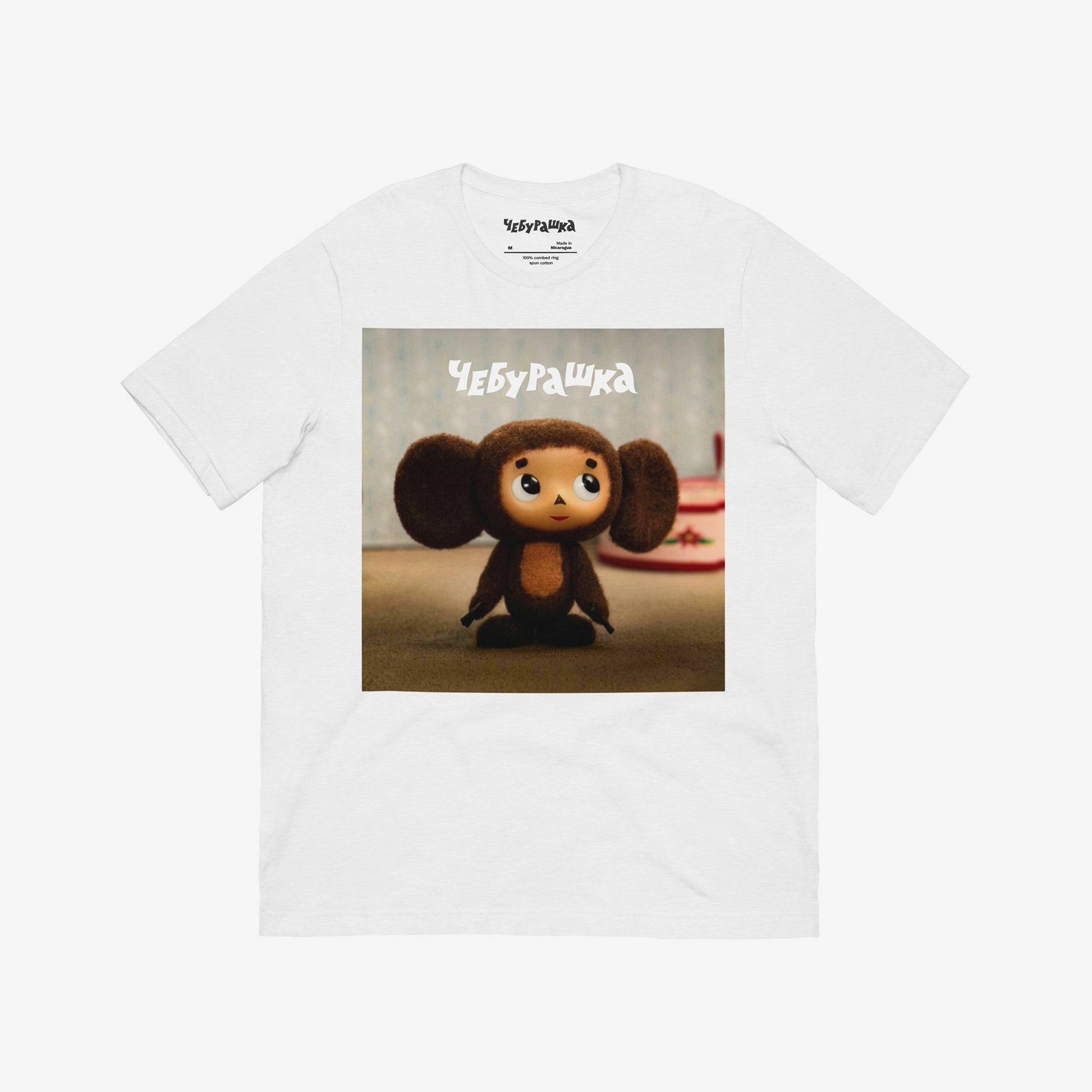 White unisex T-shirt with large print of original Soviet cartoon character Cheburashka standing cute and curious. Featuring Чебурашка logo at the of the print. Front.