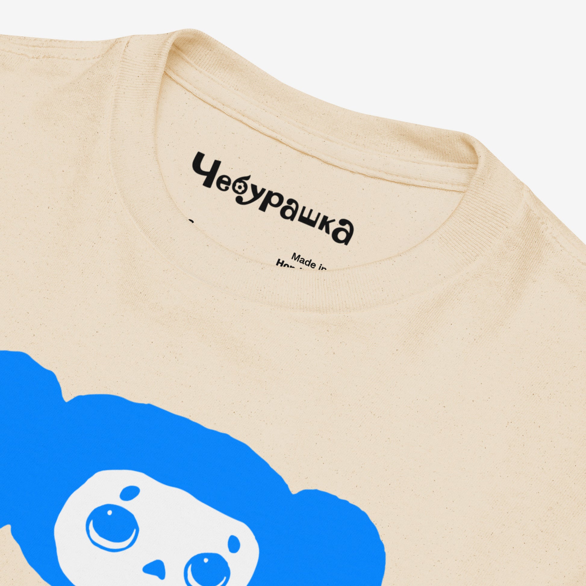 Beige unisex youth T-shirt with original Soviet cartoon character Cheburashka eating ice-cream, with logo in japanese チェブラーシカ. Closeup print details with Чебурашка logo on the necktag.