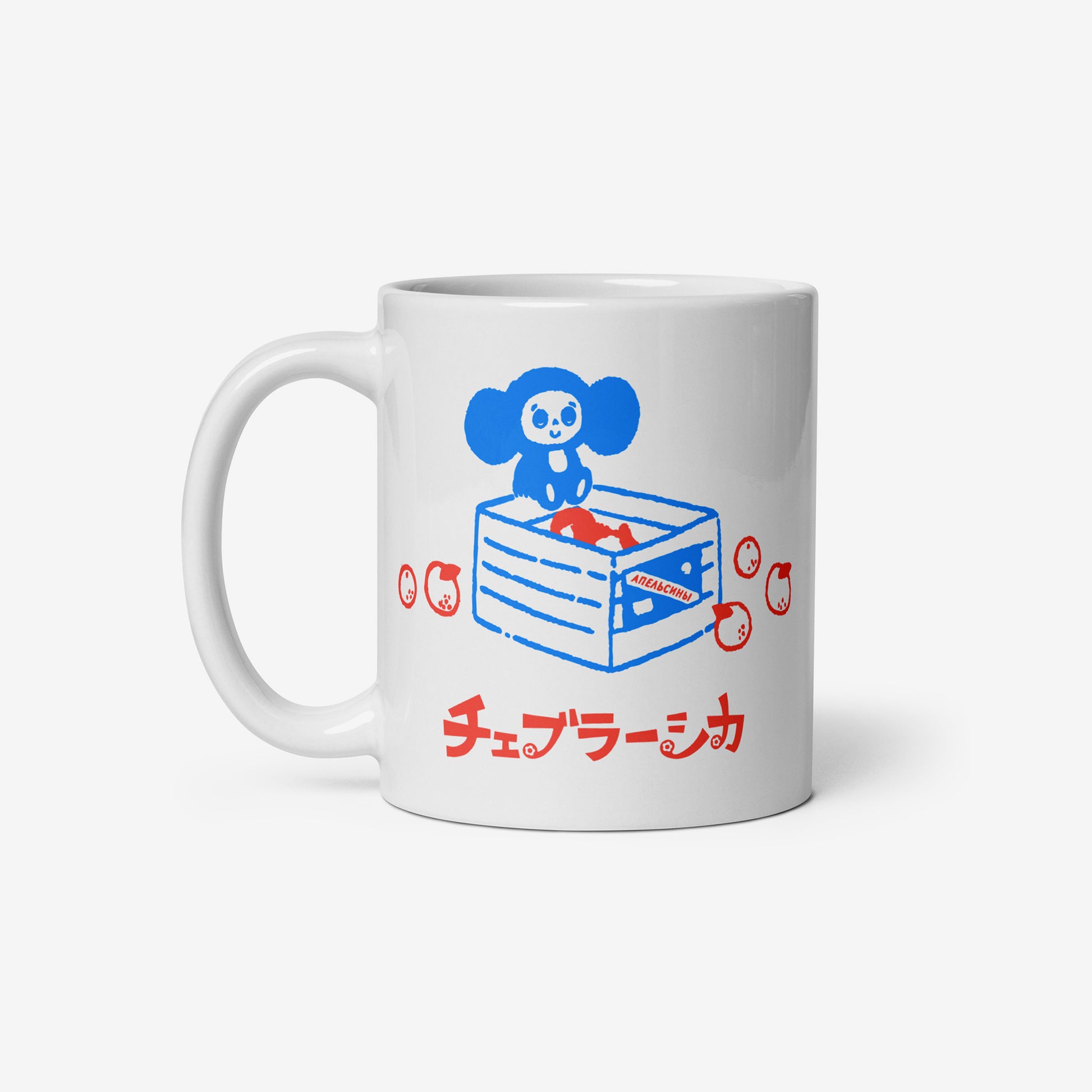 White coffee cup with Cheburashka sitting on a box of oranges and チェブラーシカ logo in red. Front.