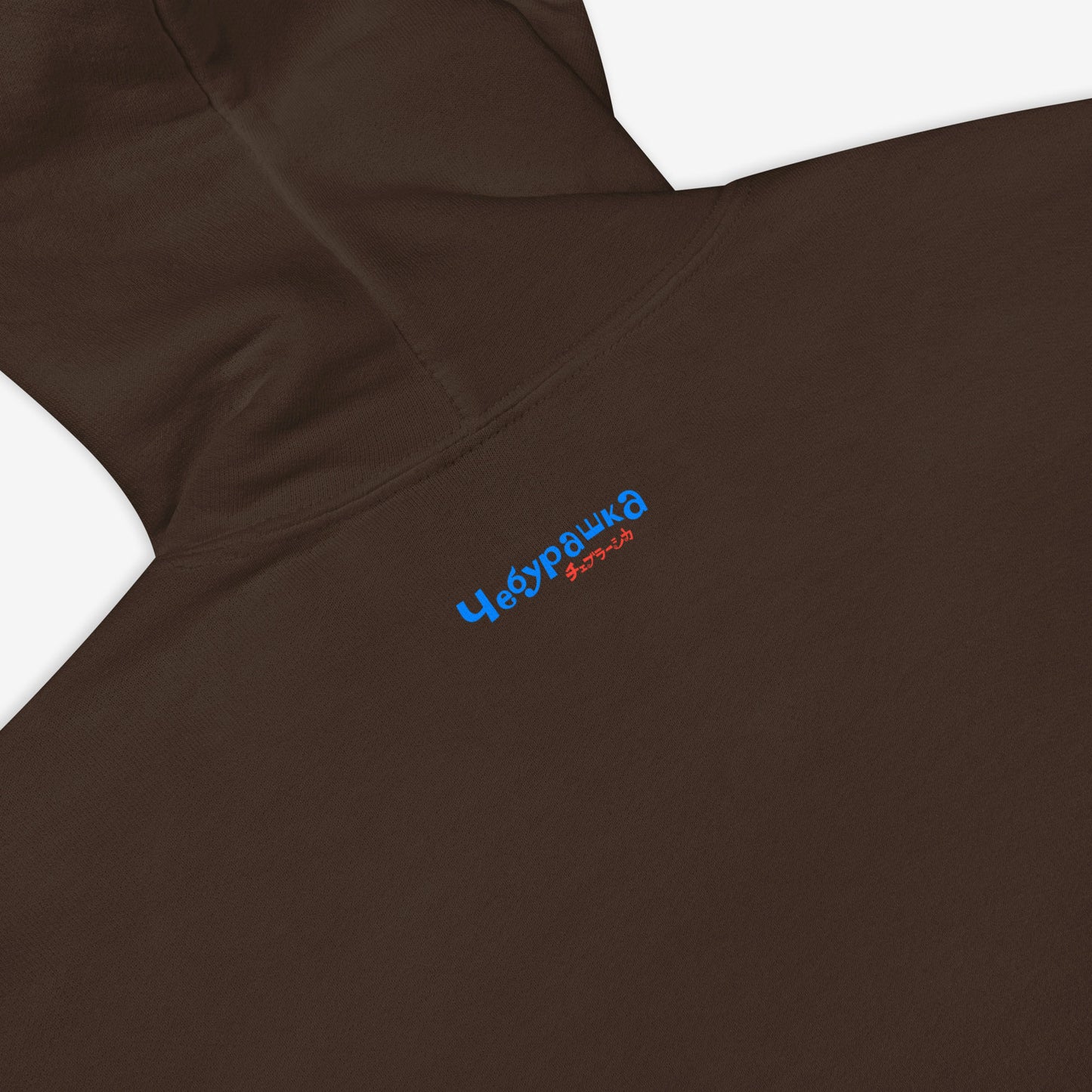 Brown unisex hoodie with minimalist graphic of Cheburashka with a birthday cake and チェブラーシカ japanese logo in red. Back side closeup with Чебурашка logo.