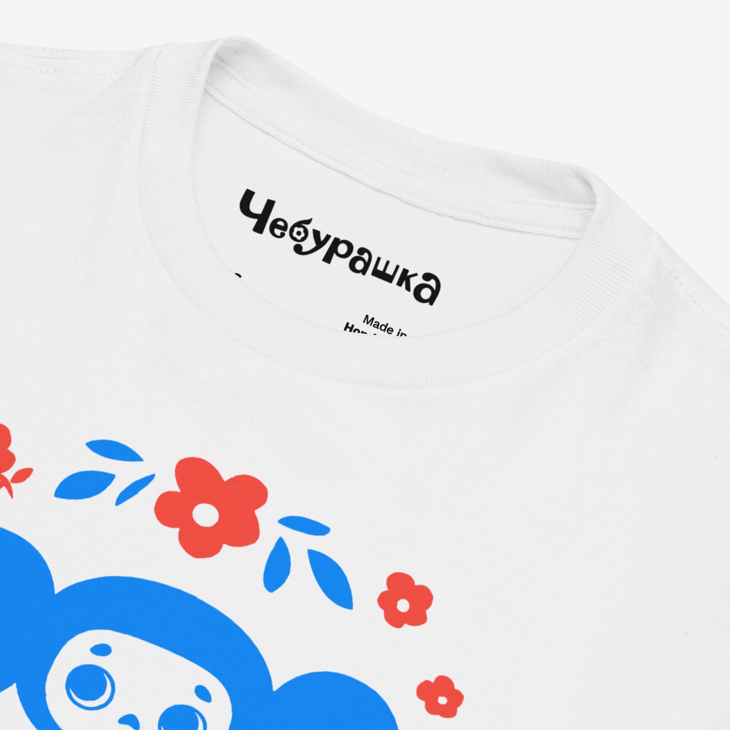 White unisex youth T-shirt with original Soviet cartoon character Cheburashka among a pattern of flowers and with logo in japanese チェブラーシカ. Closeup print details.