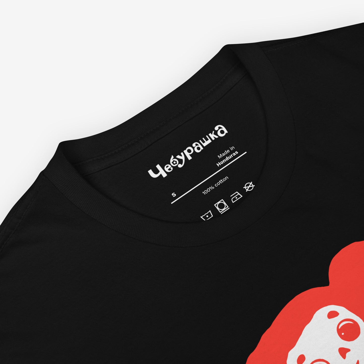 Black unisex T-shirt with minimalist graphic of Cheburashka with flowers and チェブラーシカ japanese logo in red. Closeup.