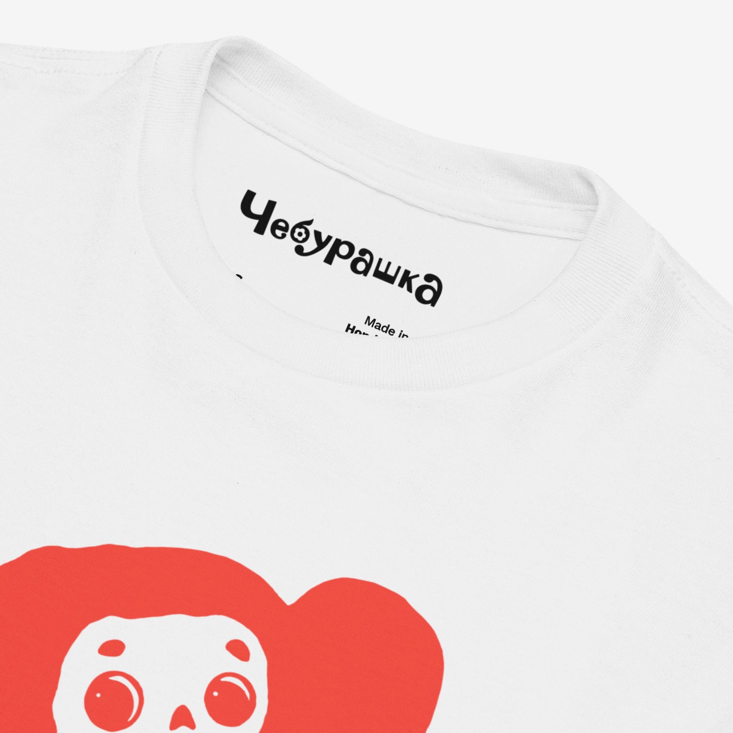 White unisex youth T-shirt with minimalist graphic of Cheburashka with flowers and チェブラーシカ japanese logo in red. Front closeup.