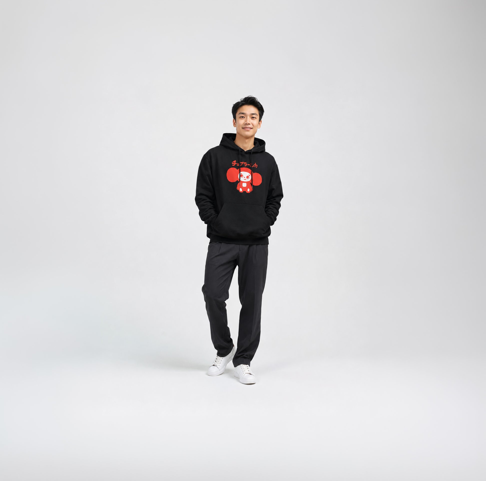 Japanese young men model wearing black unisex hoodie with minimalist graphic of original smiley Soviet cartoon character Cheburashka and チェブラーシカ logo in red.