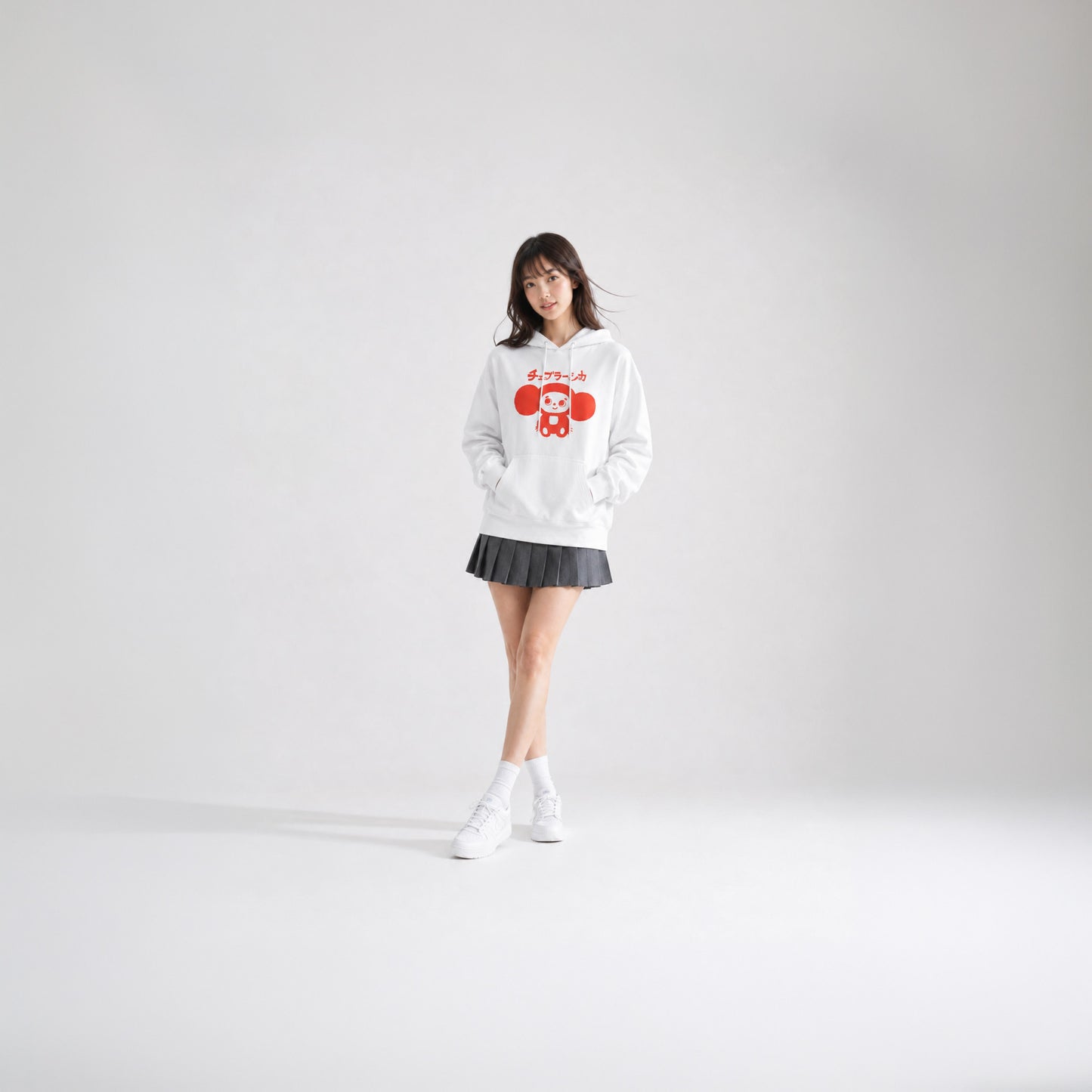 Japanese girl model wearing skirt and white unisex hoodie with minimalist graphic of original smiley Soviet cartoon character Cheburashka and チェブラーシカ logo in red.