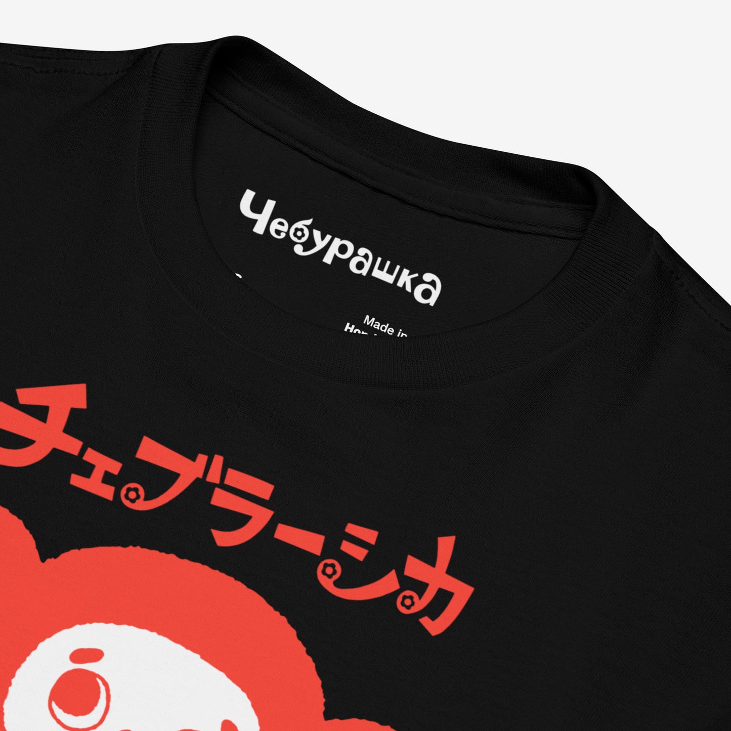 Beige unisex youth T-shirt with minimalist graphic of original smiley Soviet cartoon character Cheburashka and チェブラーシカ logo in red. Closeup print details with Чебурашка logo on the neck tag..