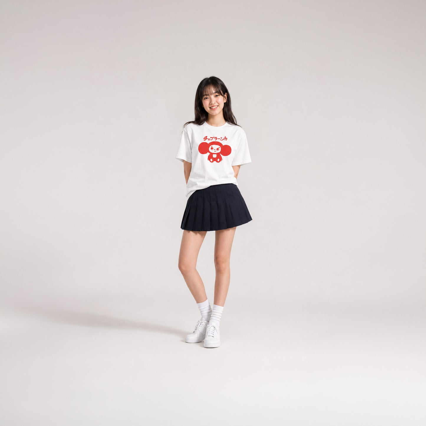 Japanese school girl model wearing skirt and white unisex youth T-shirt with minimalist graphic of original smiley Soviet cartoon character Cheburashka and チェブラーシカ logo in red.