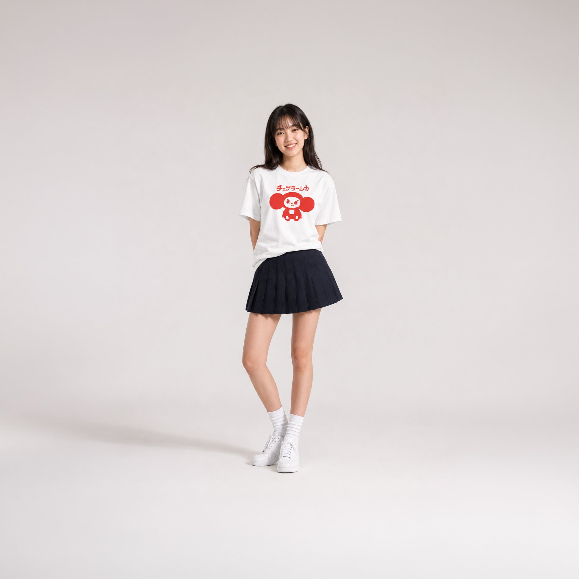 Japanese school girl model wearing skirt and white unisex youth T-shirt with minimalist graphic of original smiley Soviet cartoon character Cheburashka and チェブラーシカ logo in red.