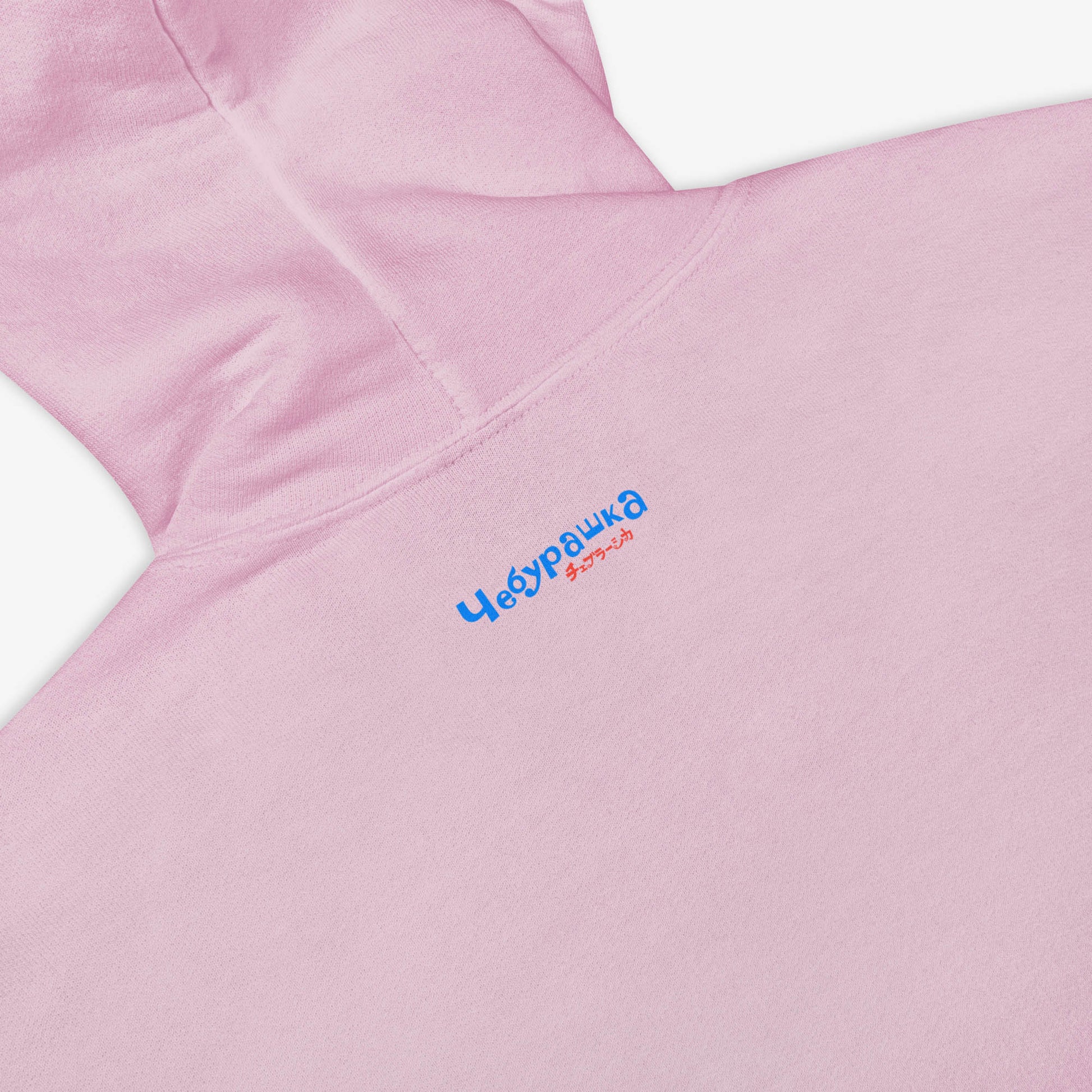 Light pink unisex hoodie with original Soviet cartoon character Cheburashka among a pattern of flowers and with logo in japanese チェブラーシカ. Back side closeup print detail with little Чебурашка logo.