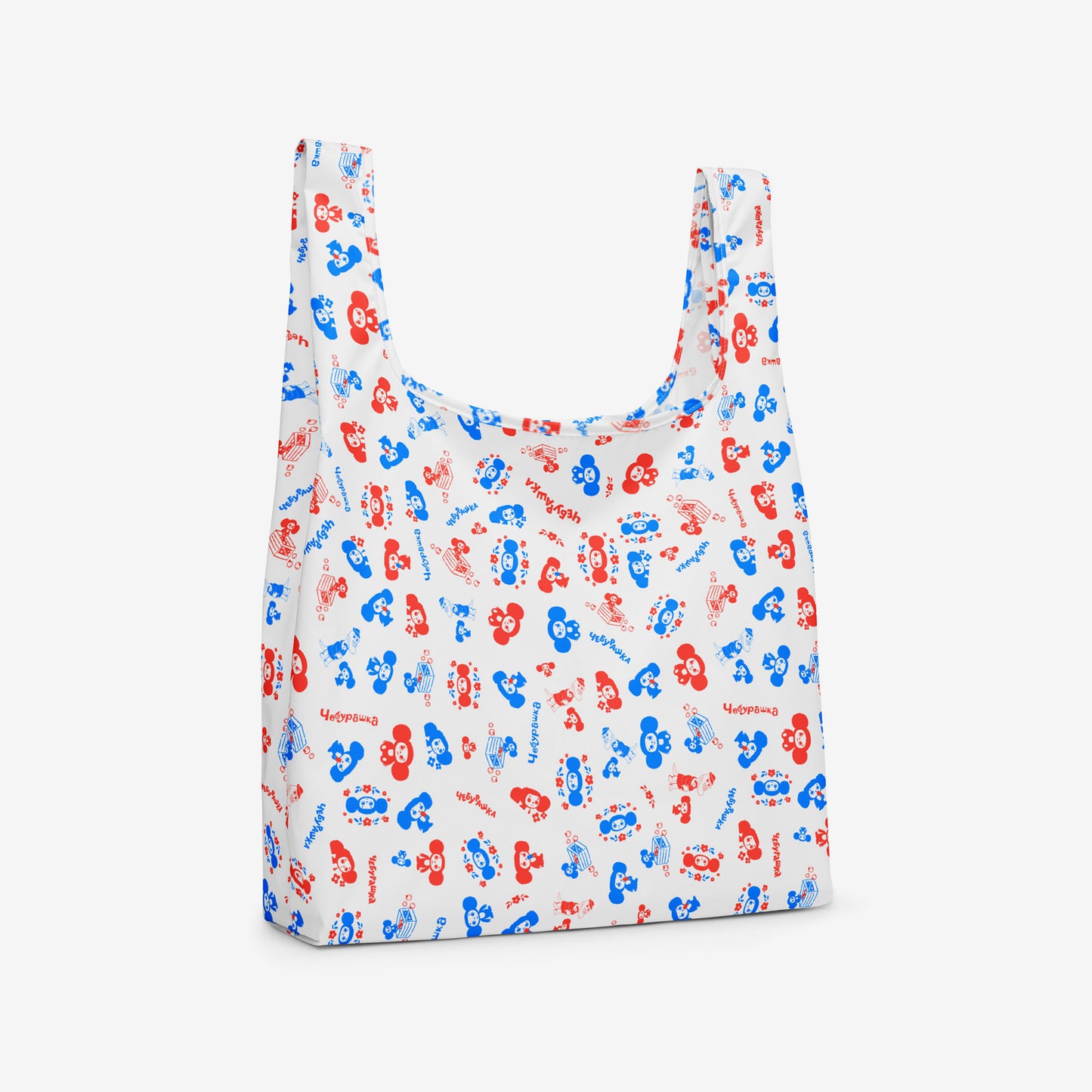 A reusable folding shopping bag with a white background and an all-over pattern of red and blue Soviet cartoon character Cheburashka. Side photo.
