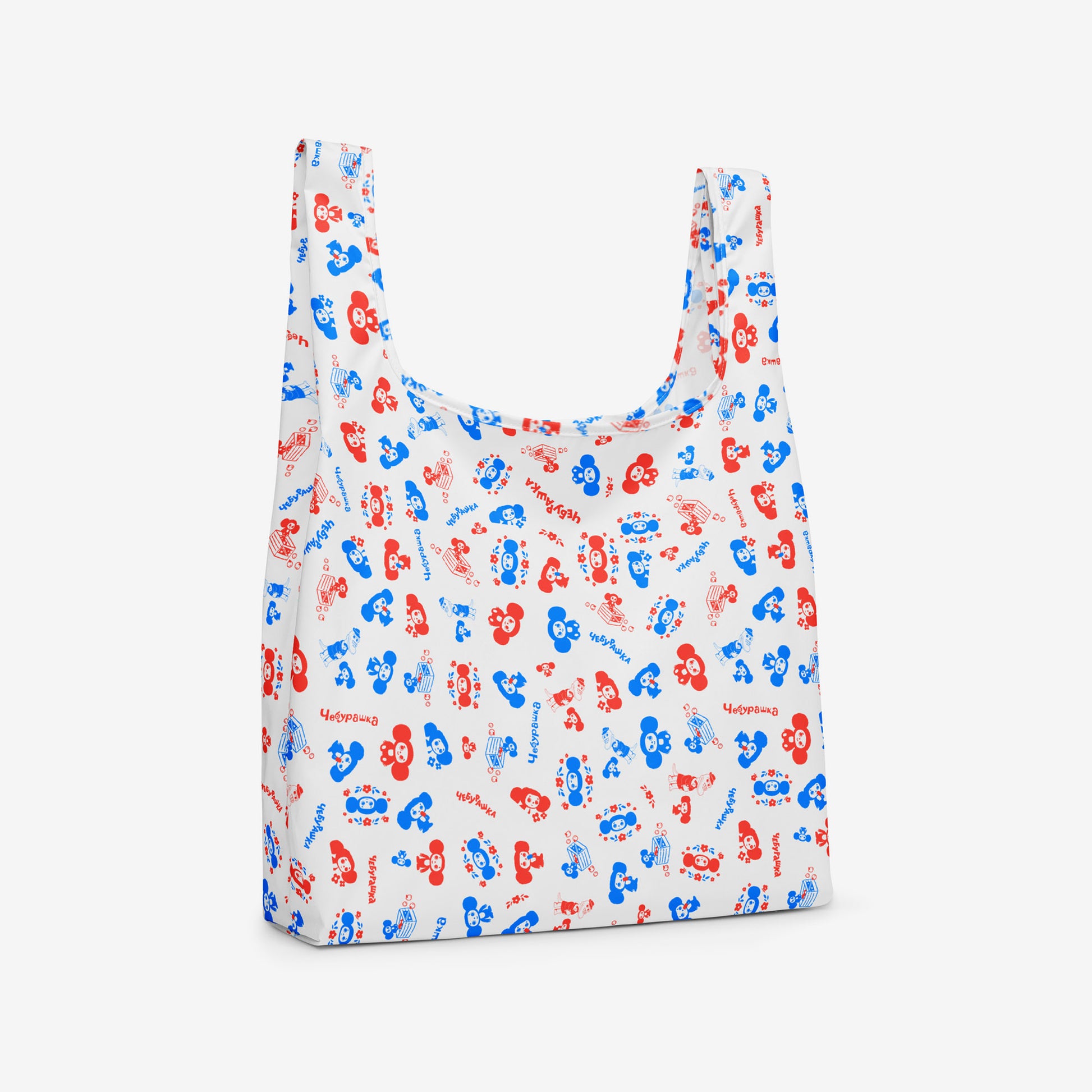 A reusable folding shopping bag with a white background and an all-over pattern of red and blue Soviet cartoon character Cheburashka. Side photo.