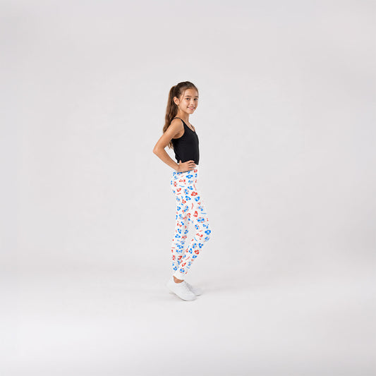 A young girl stands in profile against a white studio background, wearing white youth leggings with a colorful blue and red Soviet cartoon character Cheburashka pattern.