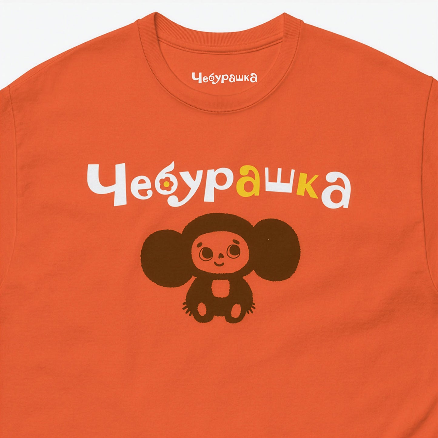 Orange unisex tee with original Soviet cartoon character Cheburashka. Lonely and smiley, with Чебурашка logo. Closeup.
