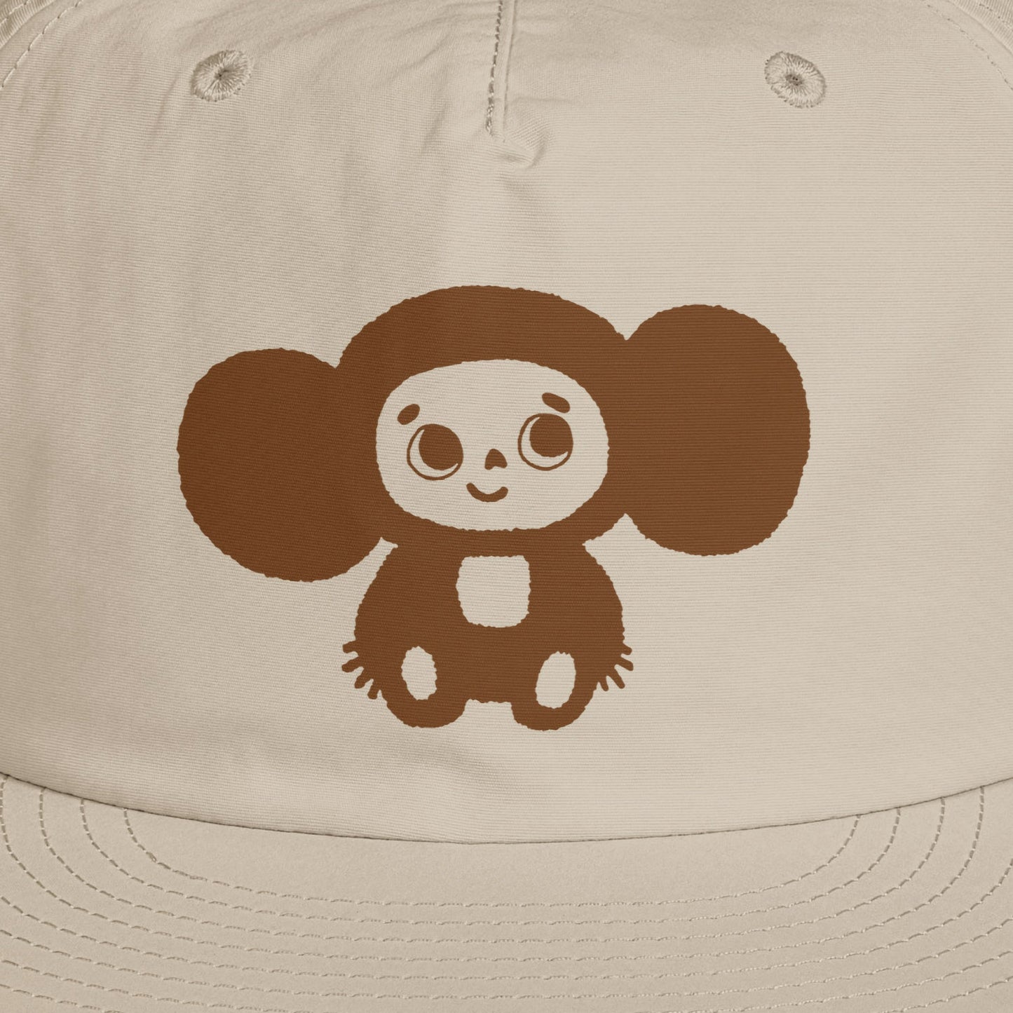A beige surf cap with a flat brim, featuring brown Soviet cartoon character Cheburashka on the front. Closeup.