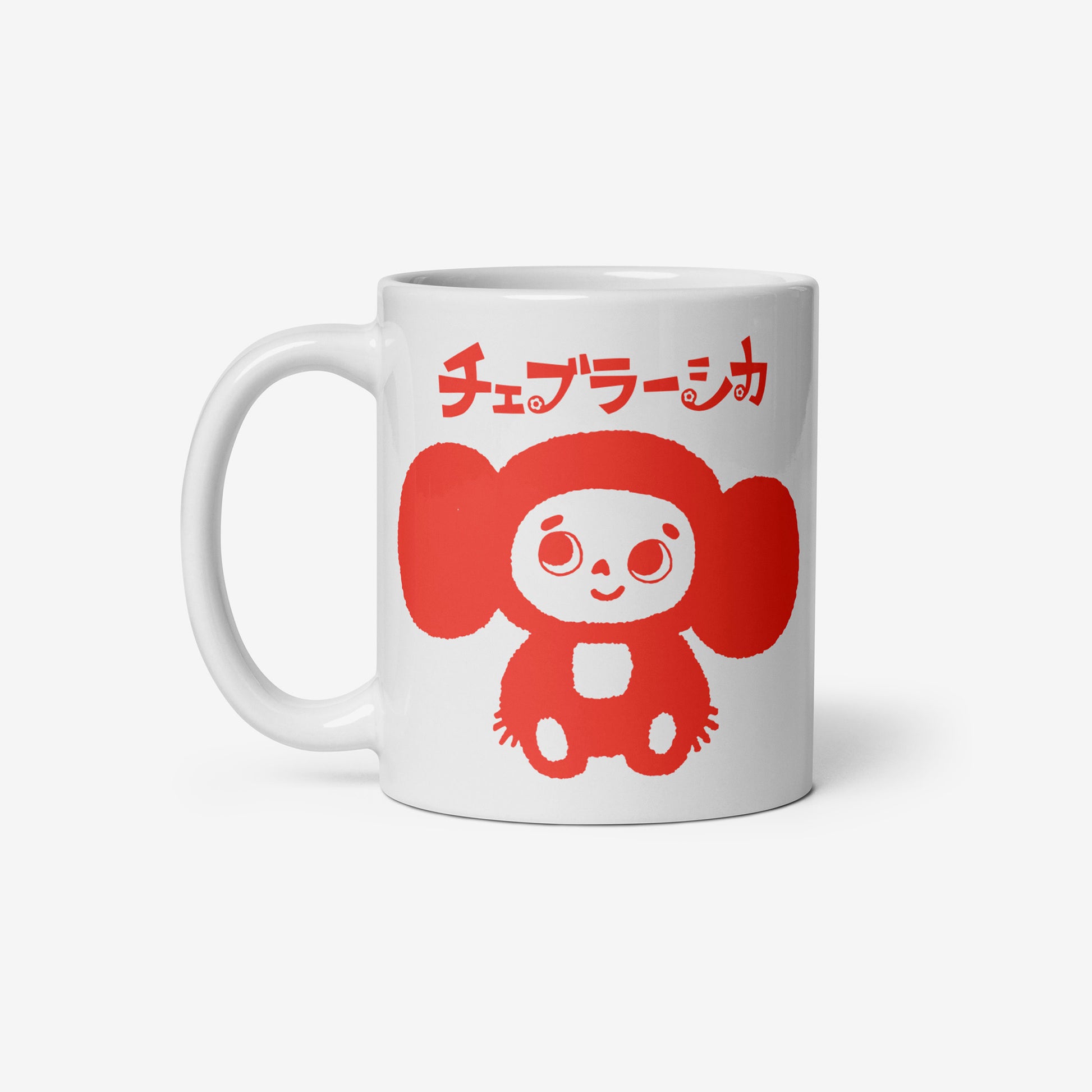 White coffee cup with minimalist graphic of smiley Cheburashka and チェブラーシカ logo in red. Front side.